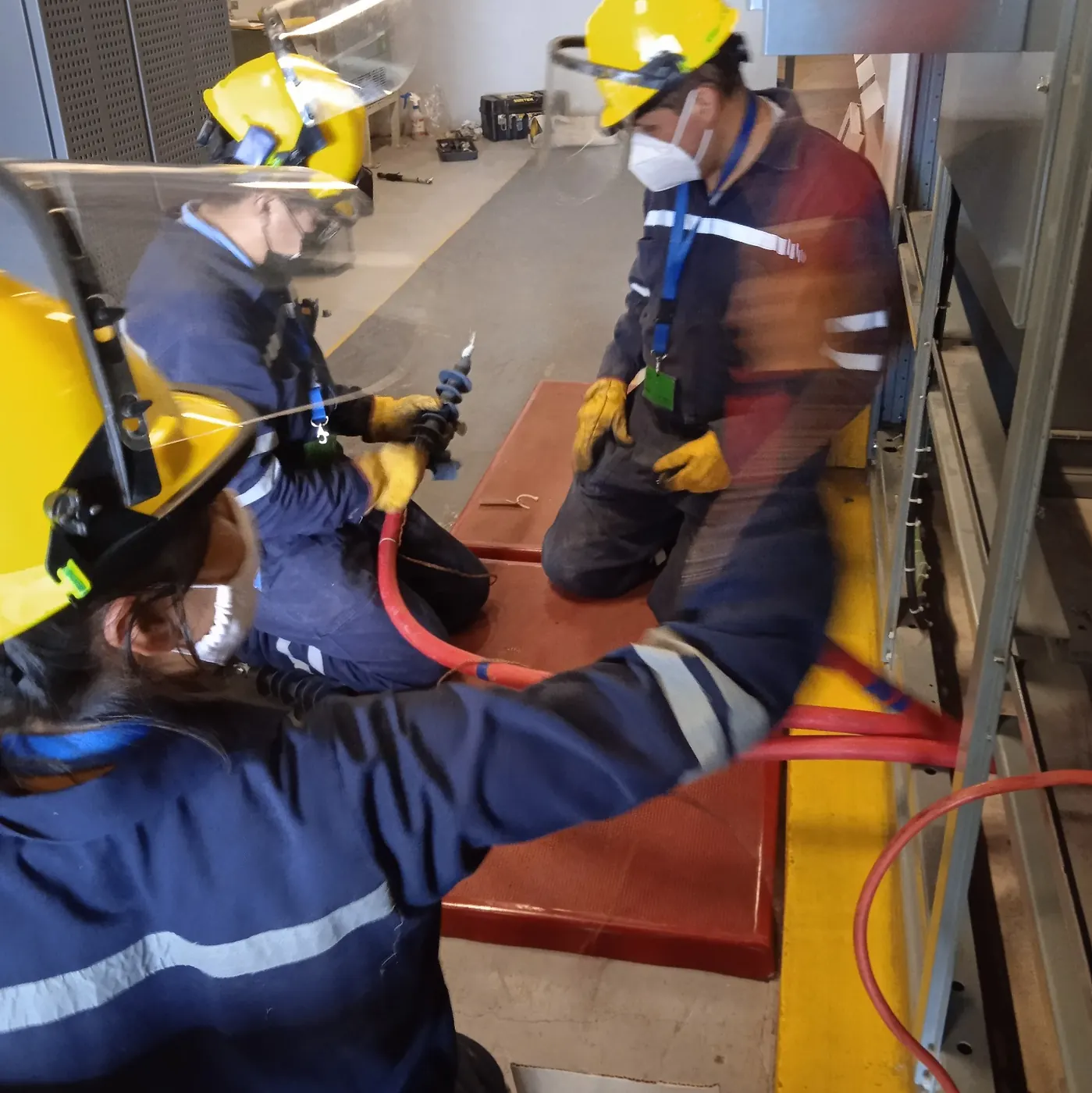 Técnicos con casco y careta de protección trabajando en una subestación con cable de potencia rojo