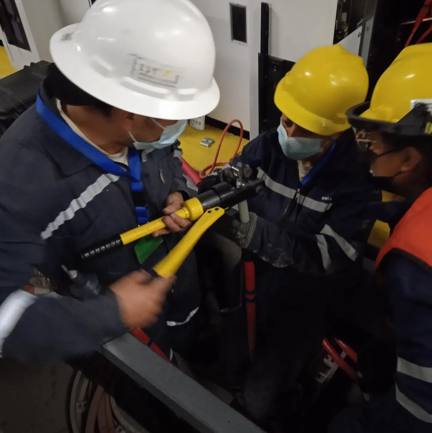 Tres técnicos usando una herramienta hidráulica para trabajar terminales de cable